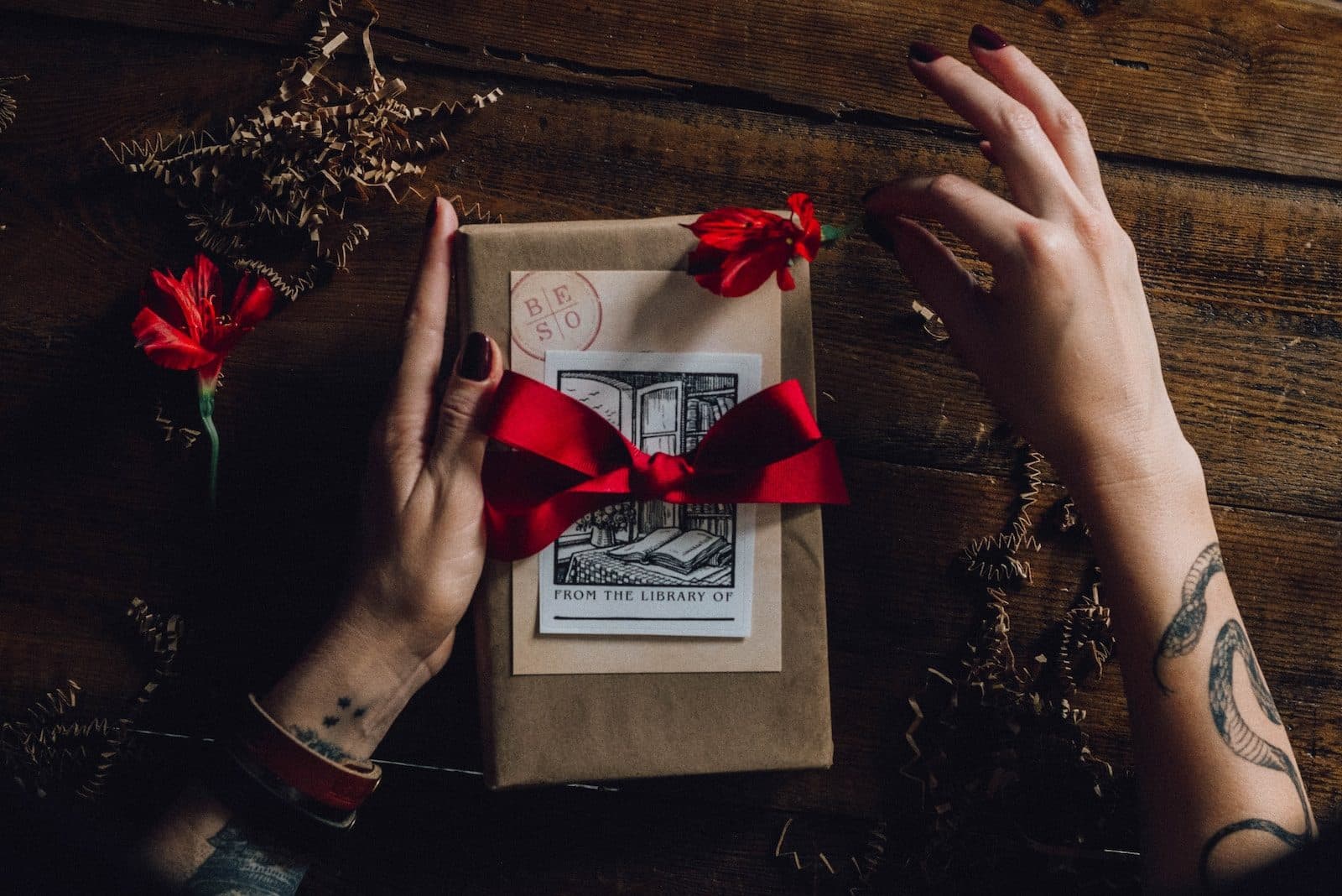 Deux mains nouant un ruban rouge autour d’un paquet cadeau en papier kraft