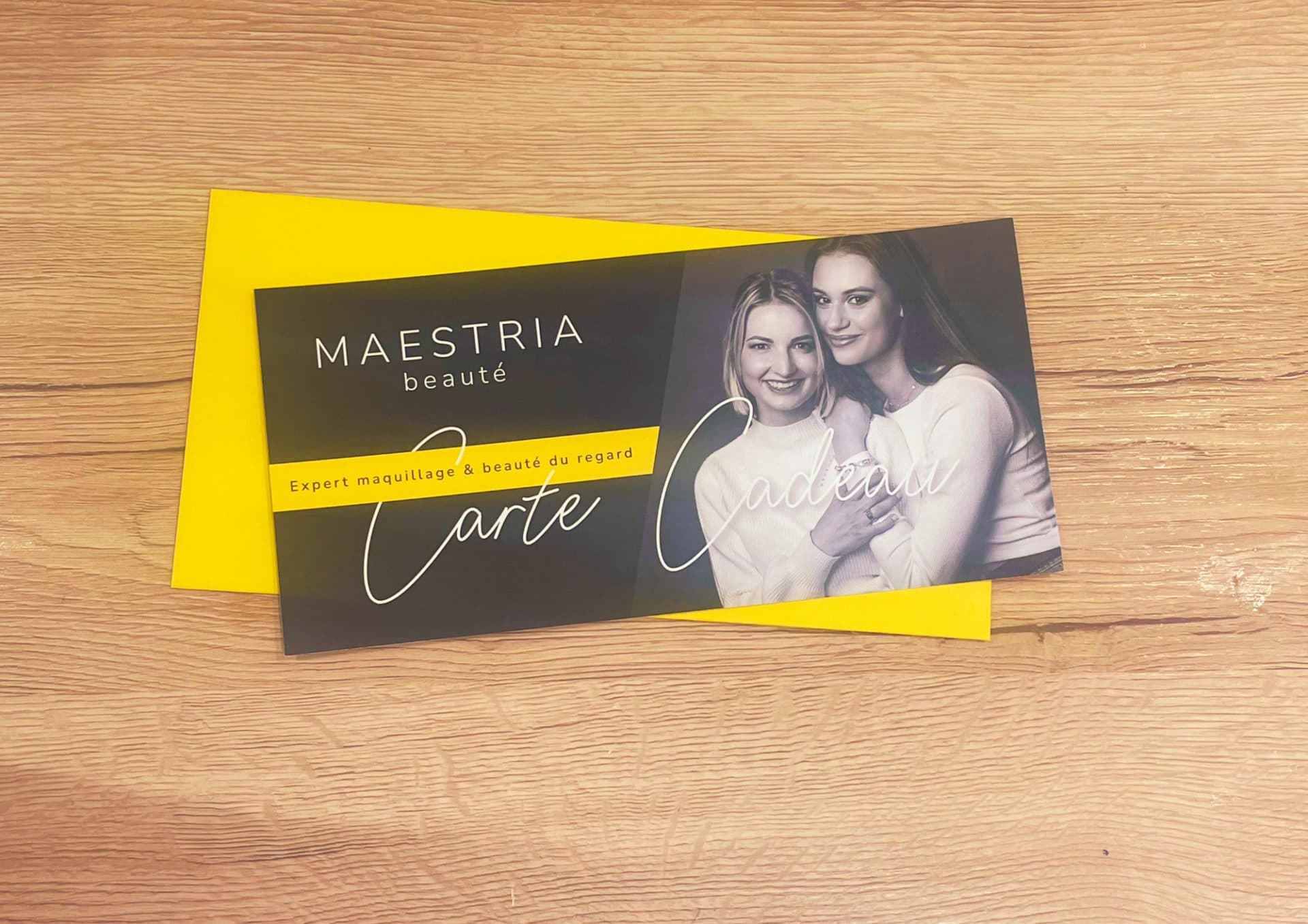 Deux cartes cadeaux Maestria Beauté, l’une noire et l’une jaune, posées sur un plan de bois